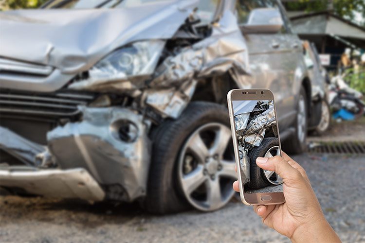 A cell phone being held up to take a picture of a terrible car accident to document it for insurance.