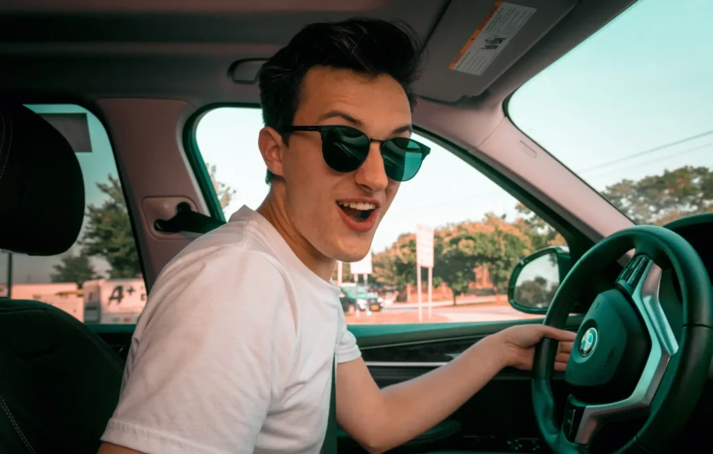 man wearing white t-shirt and sunglasses sitting on driver's seat smiling