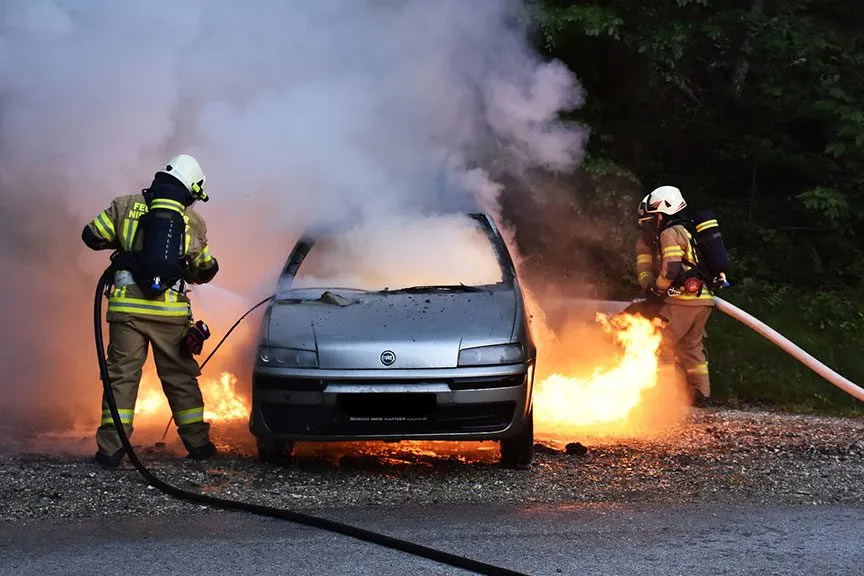 Three firefighters trying to extinguish a car on fire.