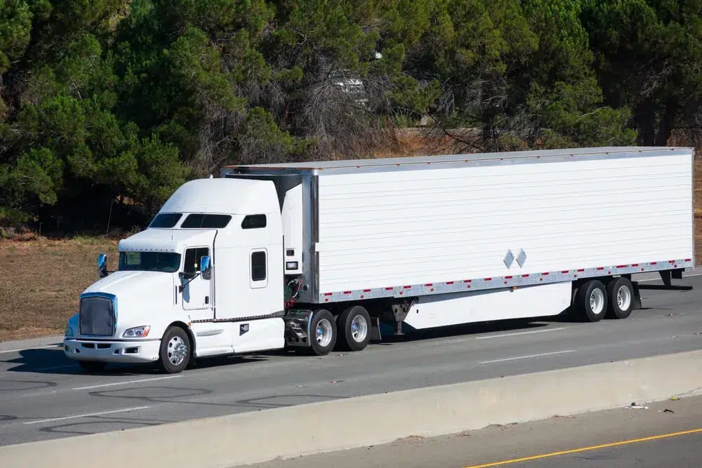 White big rig long haul semi truck transporting commercial cargo in refrigerator semi truck running alone on the eight lanes highway