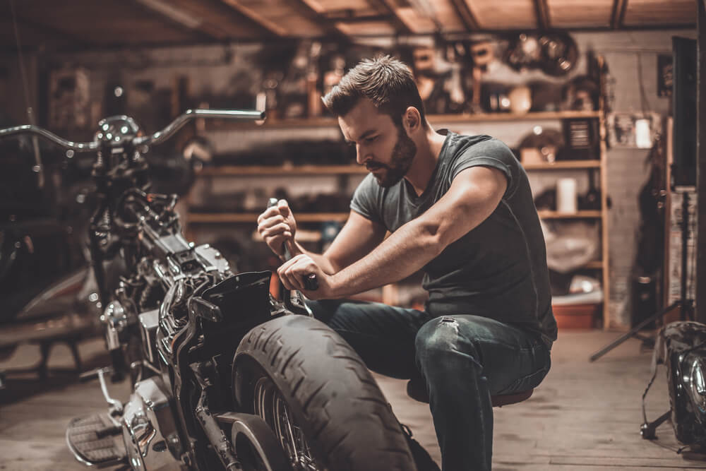 young man with PTSD repairing motorcycle in repair shop.