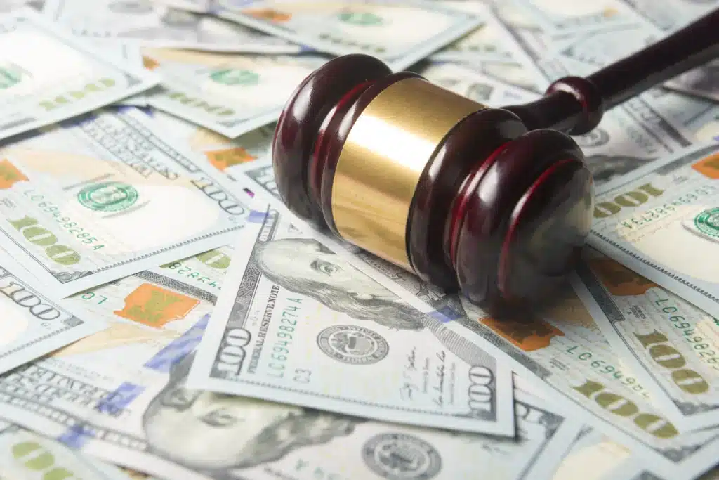 Several 100$ bills scattered across a table with a wooden gavel on top.