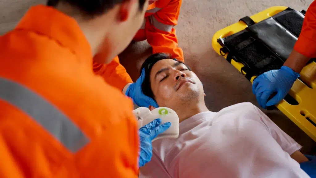 Hurt blue color worker on the floor with emergency technicians providing first-aid.