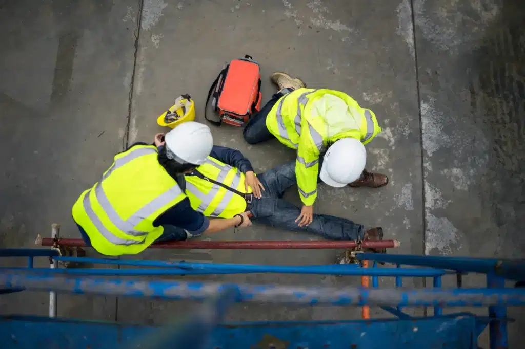 An injured worker on the ground with coworkers surrounding him.